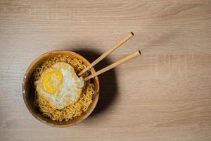 Fried Noodles and Sunny-Side Up Egg with Chopsticks on a Wooden Bowl and Wooden Table photo