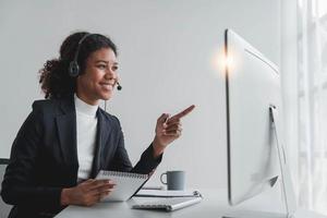 close up call center operator in wireless headset talking with customer, woman in headphones with microphone consulting client on phone in customer support service, looking at computer screen photo