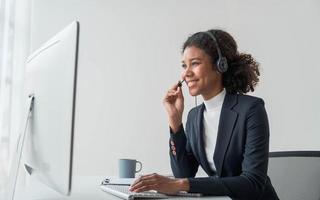 close up call center operator in wireless headset talking with customer, woman in headphones with microphone consulting client on phone in customer support service, looking at computer screen photo