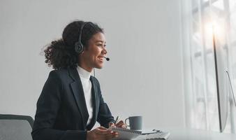 close up call center operator in wireless headset talking with customer, woman in headphones with microphone consulting client on phone in customer support service, looking at computer screen photo
