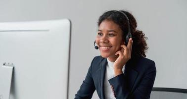 close up call center operator in wireless headset talking with customer, woman in headphones with microphone consulting client on phone in customer support service, looking at computer screen photo