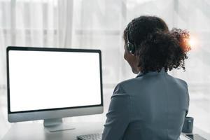 close up call center operator in wireless headset talking with customer, woman in headphones with microphone consulting client on phone in customer support service, looking at computer screen photo