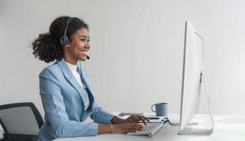 close up call center operator in wireless headset talking with customer, woman in headphones with microphone consulting client on phone in customer support service, looking at computer screen photo