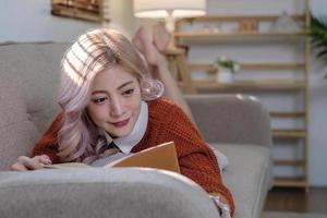 atractivo joven asiático mujer se sienta en el mínimo y cómodo vivo habitación disfrutando leyendo un libro. foto