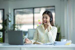 close up call center operator in wireless headset talking with customer, woman in headphones with microphone consulting client on phone in customer support service, looking at computer screen photo