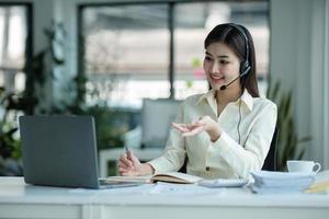 close up call center operator in wireless headset talking with customer, woman in headphones with microphone consulting client on phone in customer support service, looking at computer screen photo