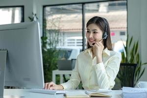 close up call center operator in wireless headset talking with customer, woman in headphones with microphone consulting client on phone in customer support service, looking at computer screen photo