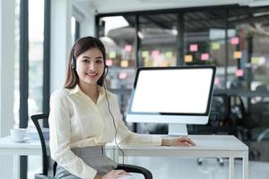 close up call center operator in wireless headset talking with customer, woman in headphones with microphone consulting client on phone in customer support service, looking at computer screen photo