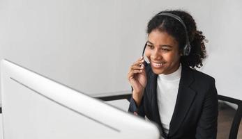 close up call center operator in wireless headset talking with customer, woman in headphones with microphone consulting client on phone in customer support service, looking at computer screen photo