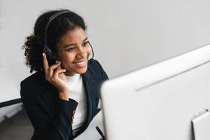 close up call center operator in wireless headset talking with customer, woman in headphones with microphone consulting client on phone in customer support service, looking at computer screen photo