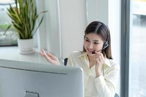 close up call center operator in wireless headset talking with customer, woman in headphones with microphone consulting client on phone in customer support service, looking at computer screen photo