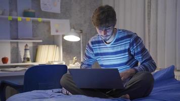 Correspondence of young man sitting in bed at night chatting on laptop. In the bedroom, the young man is chatting by texting on the laptop. He's happy. video