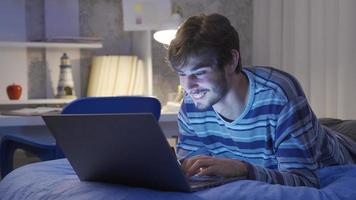 Correspondence of young man sitting in bed at night chatting on laptop. In the bedroom, the young man is chatting by texting on the laptop. He's happy. video