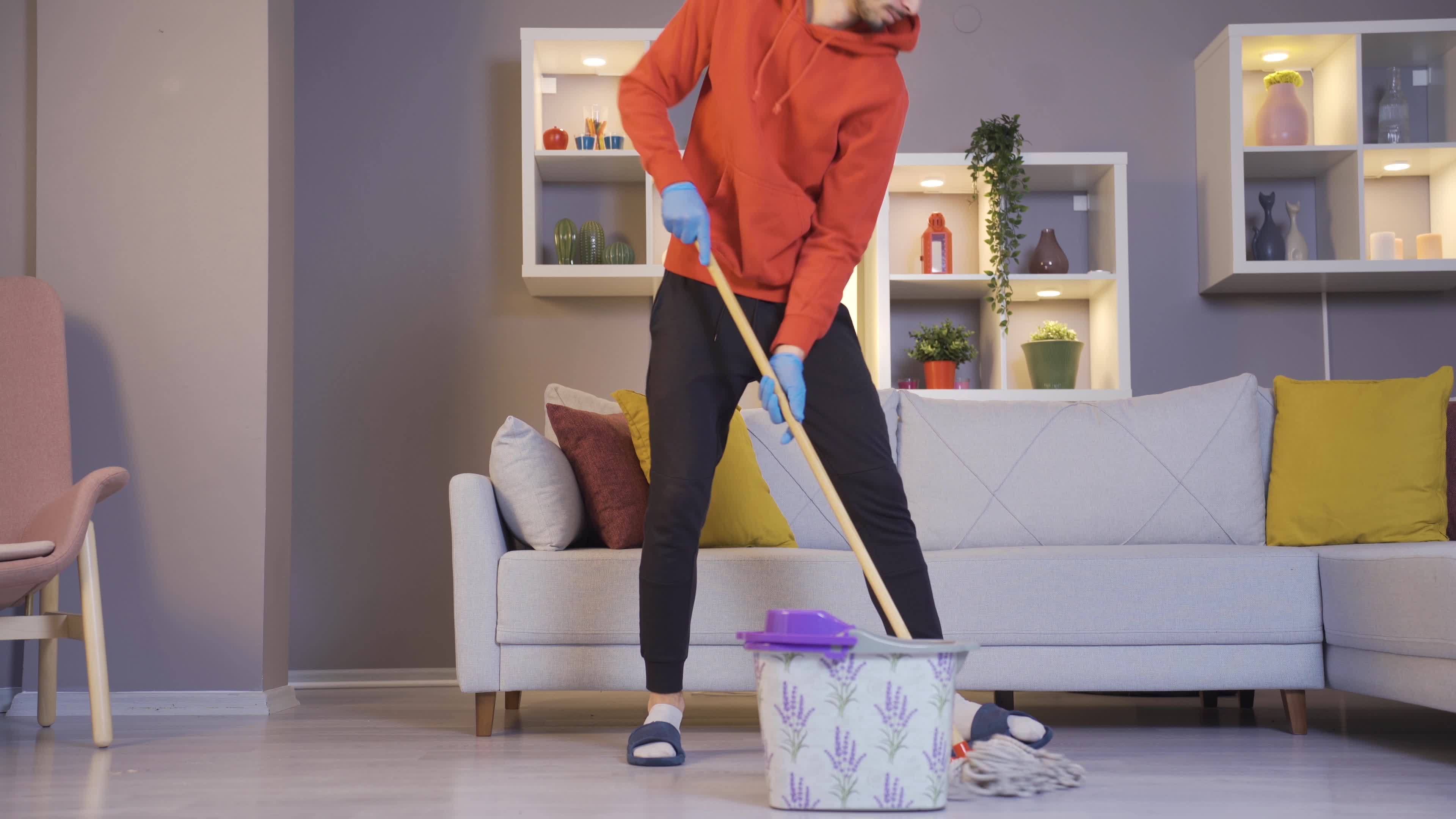 The man cleaning the house while having fun is dancing. Funny young man