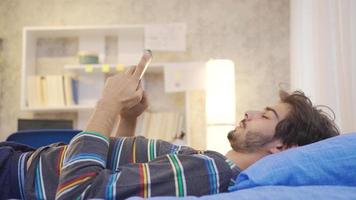 Phone addicted young man texting on the phone in his bed. Phone addicted young man lying in bed at home, dozing off and dropping the phone from his hand. video