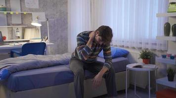 joven hombre infeliz en su habitación. joven hombre sentado en su cama es infeliz y deprimido. video