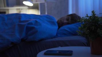 jovem homem dormindo dentro cama às casa acorda acima para desativar a alarme. adolescente acorda acima e voltas fora a alarme relógio em a Smartphone. video