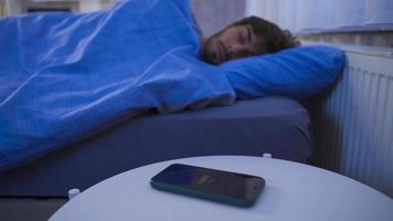 Teenager Wakes Up and Turns Off The Alarm Clock On The Smartphone. The Bedroom Cell Phone Showing Six A.M. alarm goes off and the young man turns it off and continues to sleep. video