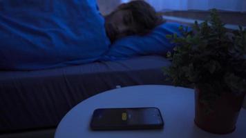 The sleeping man wakes up early in the morning to the sound of an alarm. Young man sleeping in bed at home wakes up to deactivate the alarm. video