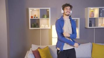 Young man listening to music wearing headphones at home, dancing, having fun. Cheerful young man listens to moving music on headphones and dances. Listen to music. video