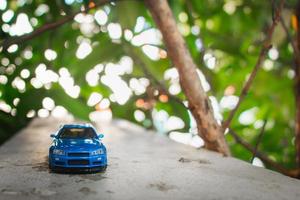 Concept for nature adventure. After some edits, a photo of blue toy car placed near a tree.