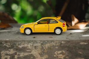 A photo of a yellow toy car placed near a tree, after some edits. Concept for nature adventure.