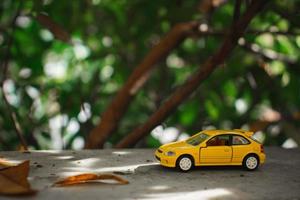 A photo of a yellow toy car placed near a tree, after some edits. Concept for nature adventure.