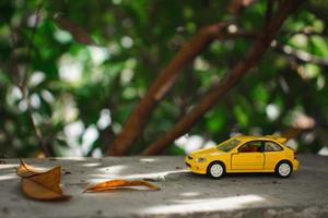 A photo of a yellow toy car placed near a tree, after some edits. Concept for nature adventure.