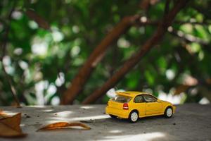 A photo of a yellow toy car placed near a tree, after some edits. Concept for nature adventure.