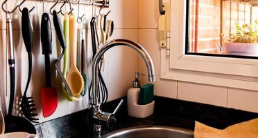 A kitchen sink with a faucet and kitchen utensils hanging from the wall. photo
