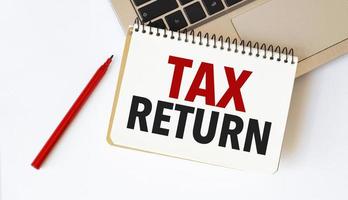 Laptop, red pen and notepad with text tax return in the white background photo