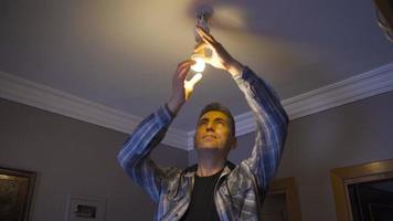 Changing the bulb. Saving bulb. The man who replaces the yellow light bulb burning on the ceiling with a white light bulb. video