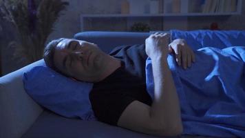 Sleep problem. Middle-aged man trying to sleep on the sofa at night. video