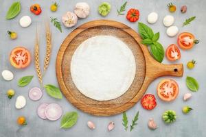 The ingredients for homemade pizza with wooden pizza tray set up on grey concrete background. top view photo