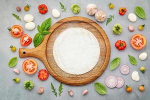 The ingredients for homemade pizza with wooden pizza tray set up on grey concrete background. top view photo