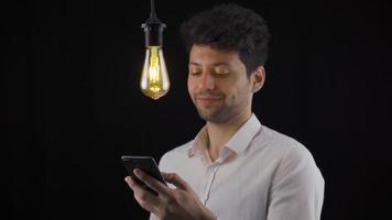 The man looking at the phone has a new idea and the lamp turns on. Eureka Male hand looking at the phone finds a new idea, invention, solution and the lamp turns on. video