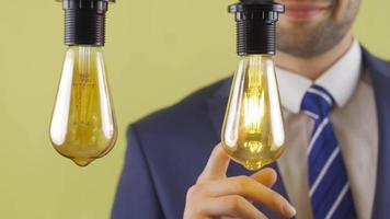 Businessman prefers one of the idea lamps. Businessman choosing one of the two idea lamps is touching the lamp. video