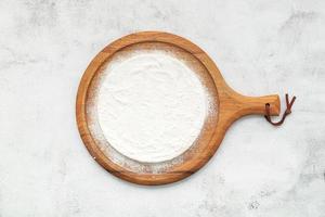 Pizza dough in wooden pizza platter set up on white concrete. Pizza tray on white concrete background flat lay and copy space. photo
