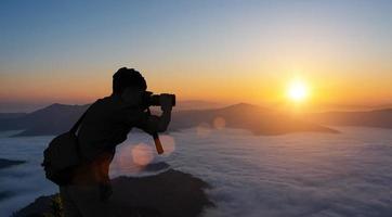 silueta de masculino fotógrafo tomando imagen en contra puesta de sol cielo antecedentes. foto