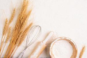 Flour in bowl and wheat grains with wheat ears, barley, cooking, bread, and cookies, arranged on the table in a rustic kitchen, top view. photo