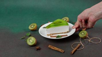 dell'uomo mano mette su piatto con fetta di torta di formaggio con Kiwi. decorato con cannella bastoni, badiano, menta le foglie video