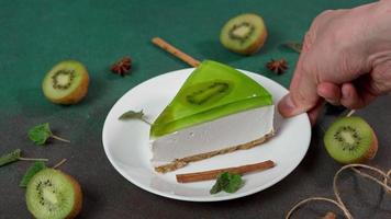 Man's Hand Puts up plate with Slice of Cheesecake with Kiwi. Decorated with cinnamon sticks, badyan, mint leaves