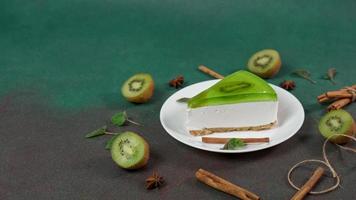 Homemade Cheesecake with Kiwi in a white plate on a Green background. Decoreted with slice of kiwi, cinnamon stick and leaves mint. Copy space video