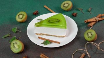 vicino su di fetta torta di formaggio con Kiwi. decorato con fetta di kiwi, cannella bastoni, badiano, menta le foglie video