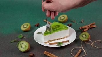 do homem mão com garfo rompe fora peça do bolo de queijo com kiwi. decorado com canela Gravetos, badyan, hortelã folhas em verde fundo video