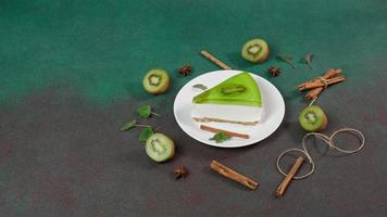 Cheesecake with Kiwi, cinnamon stick and leaves mint on a green background. Copy cpase for text video