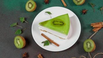 fatti in casa torta di formaggio con Kiwi nel un' bianca piatto su un' verde sfondo. decorato con fetta di kiwi, cannella bastone e le foglie menta video