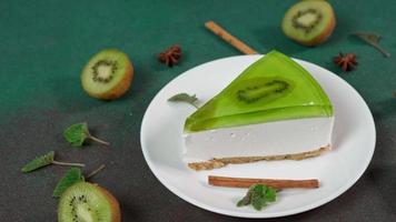 vicino su di fetta torta di formaggio con Kiwi. decorato con fetta di kiwi, cannella bastoni, badiano, menta le foglie video