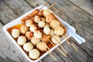 Meat ball , fish ball and sausage hotdog grilled in stick on tray with wooden background Thai style food photo