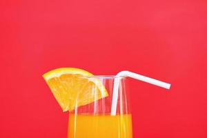 Orange juice summer glass with piece orange fruit on red background photo